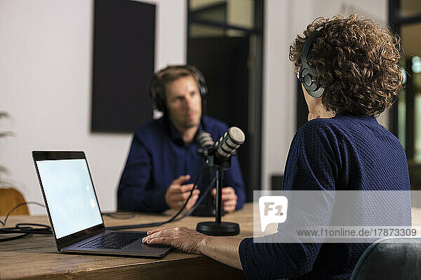 Presenter wearing headset interviewing guest in recording studio
