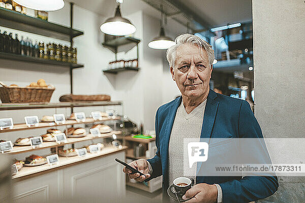 Senior businessman with coffee cup and mobile phone in cafe