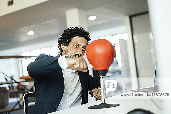 Dedicated businessman punching speed bag in office