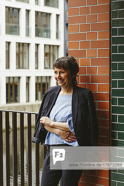 Cheerful mature woman with crossed arms leaning on wall
