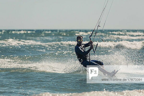 Man kiteboarding in sea splashing water on sunny day