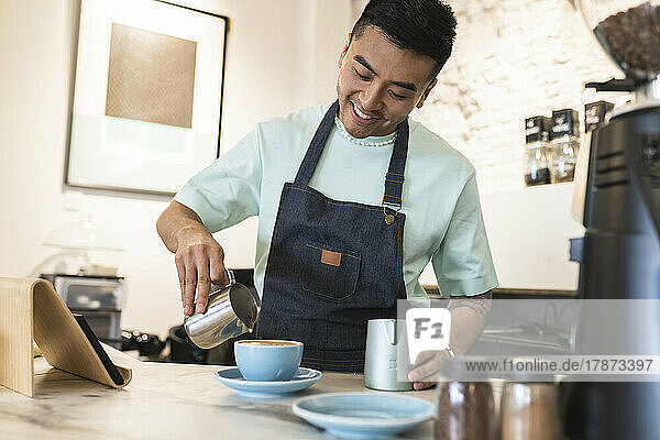 Happy young man wearing apron preparing coffee in cafe