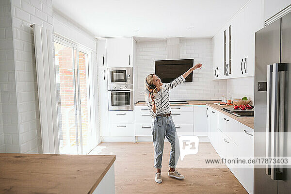 Young woman with headphones dancing in kitchen at home