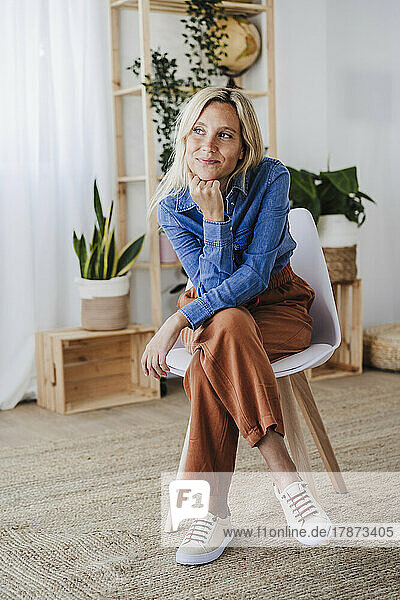 Contemplative blond woman with hand on chin sitting at home