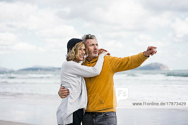 Glücklicher reifer Mann zeigt auf Frau  die am Strand steht