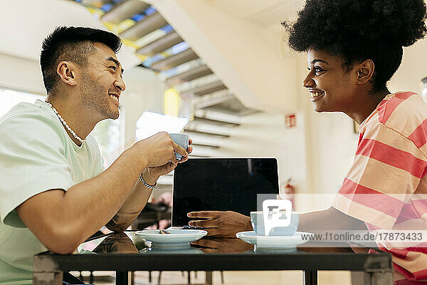 Smiling young man and woman talking with each other sitting at table in cafe