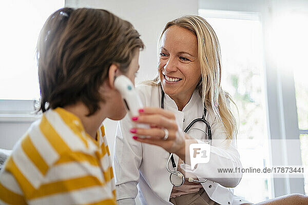 Smiling female doctor examining boy taking his temperature