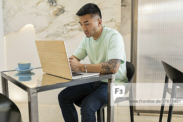 Young man sitting with laptop at table in coffee shop