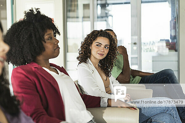Smiling young businesswoman looking at colleague sharing ideas in office