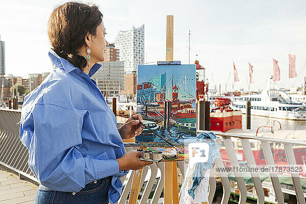 Thoughtful painter holding palette painting at harbor