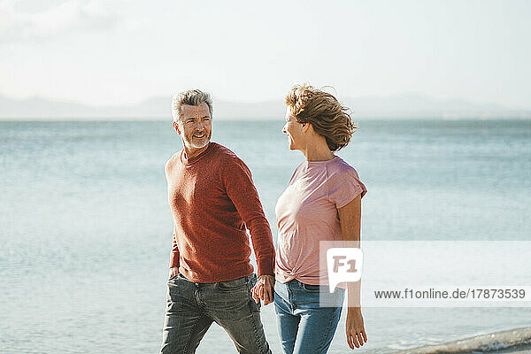 Glücklicher Mann und Frau halten sich an den Händen und gehen am Strand entlang