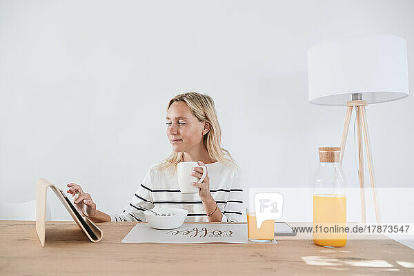 Woman having coffee and using tablet PC at home