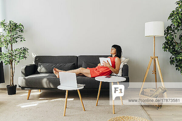 Woman with tablet PC lying on sofa in living room