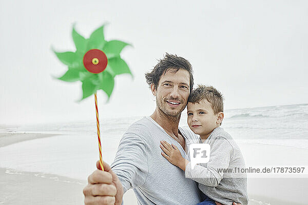 Father carrying son on the beach holding green pinwheel