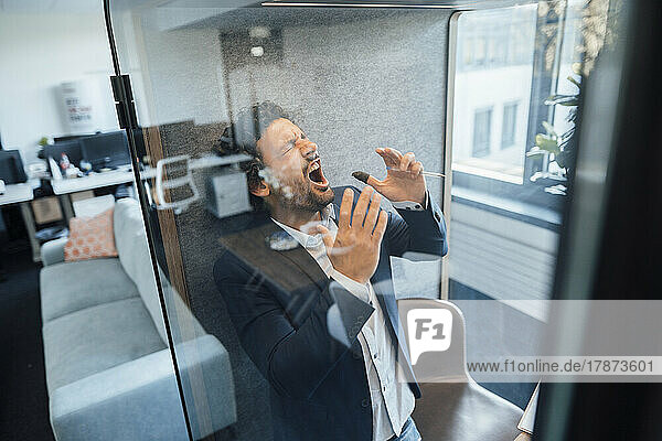 Angry businessman shouting in soundproof cabin at office
