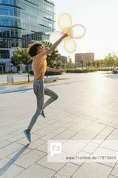 Happy woman playing with balloons at footpath