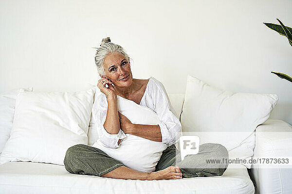 Smiling woman with cushion on sofa in living room