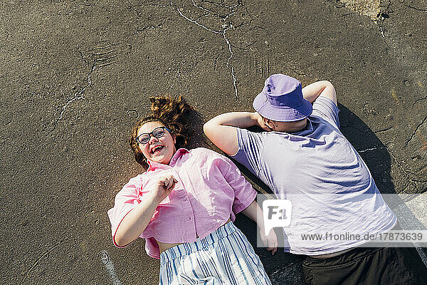 Brother and sister with down syndrome lying on footpath on sunny day