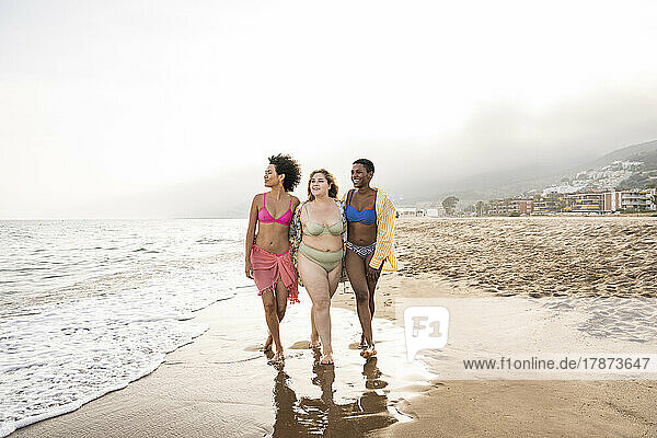 Multiracial friends walking together on shore at beach