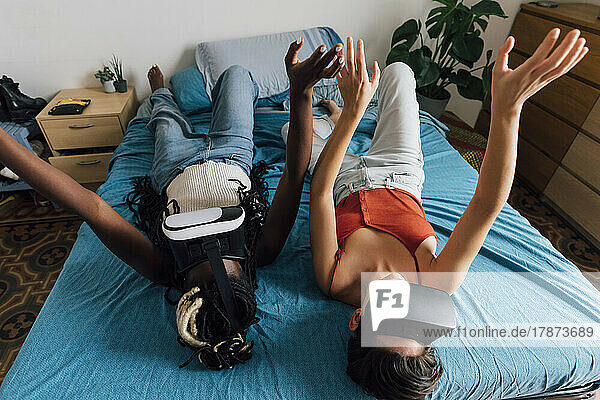Lesbian couple wearing VR glasses lying on bed at home