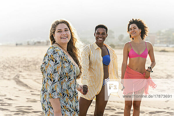 Lächelnde  gemischtrassige Freunde  die Händchen haltend am Strand stehen