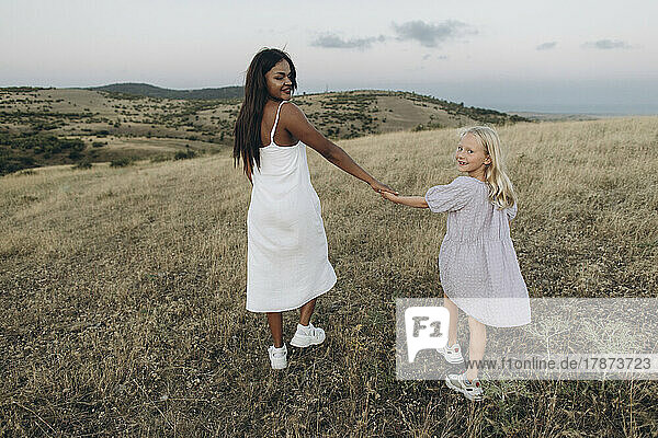 Smiling woman and girl holding hands walking in meadow