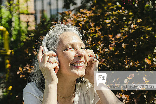 Happy woman adjusting wireless headphones in park