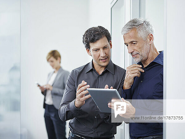 Businessman with colleague discussing over tablet PC at doorway in office