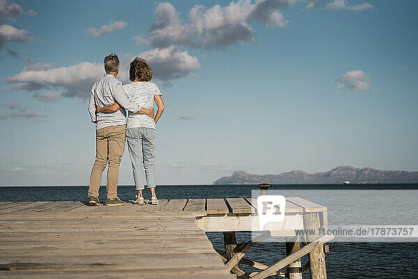 Loving mature couple with arms around each other standing on jetty