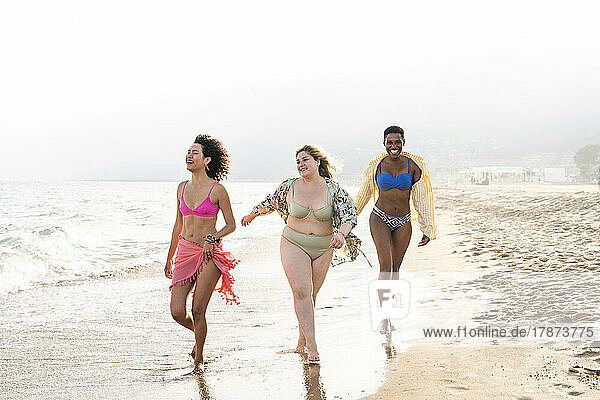 Multiracial friends in swimwear walking near seashore at beach