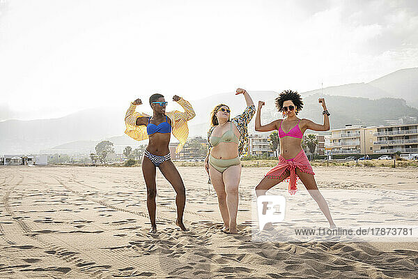 Multiracial friends flexing muscles at beach