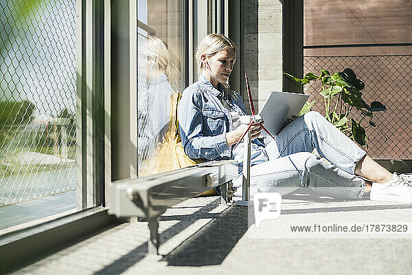 Businesswoman using tablet PC sitting by wind turbine model in office