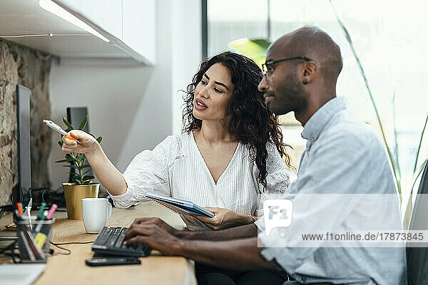 Businesswoman pointing at computer monitor sitting by businessman at office