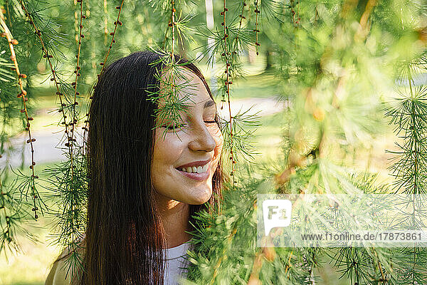 Smiling woman with eyes closed amidst plants in park