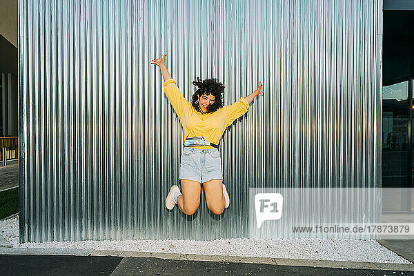 Cheerful woman jumping in front of corrugated wall