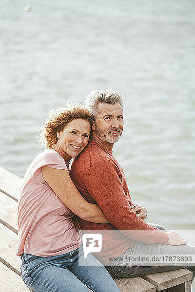 Happy woman with man sitting on jetty in front of sea