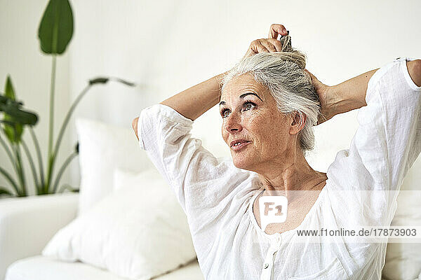 Mature woman tying hair in living room