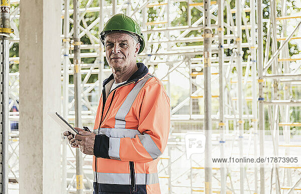 Senior contractor holding tablet PC standing in front of scaffolding