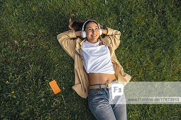 Smiling woman lying with hands behind head at park