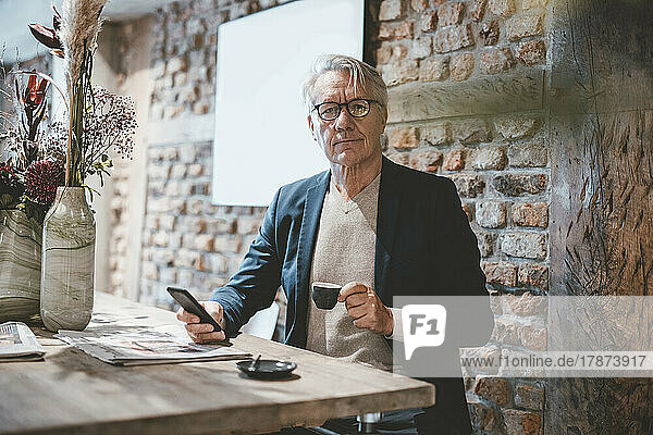 Businessman with smart phone having coffee in cafe