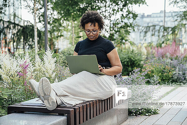 Lächelnde Geschäftsfrau mit Laptop auf Bank sitzend