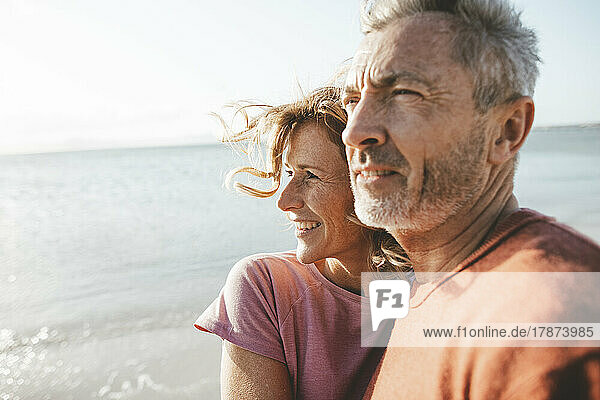 Smiling mature man with woman at beach on sunny day