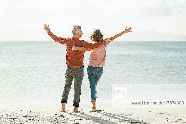 Mature couple with arms outstretched standing on shore at beach