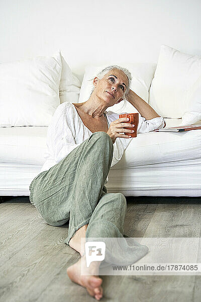 Thoughtful woman with coffee mug leaning on sofa