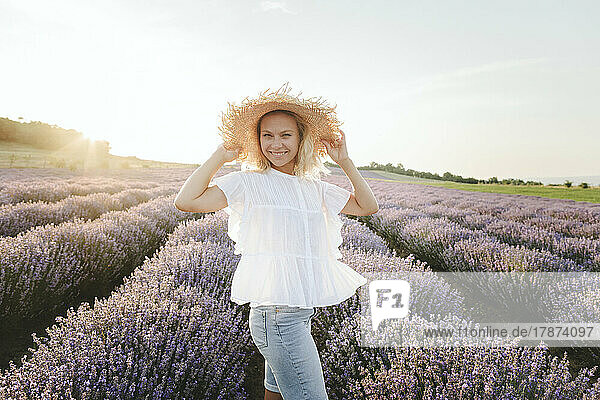 Happy woman wearing hat standing in lavender field