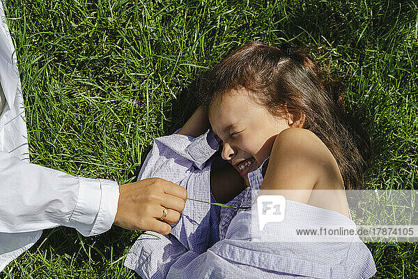 Hand of mother by daughter lying with eyes closed on grass
