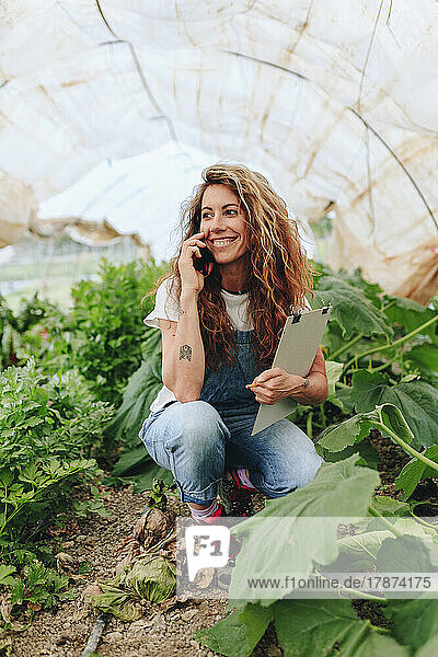 Happy farmer talking on smart phone at greenhouse