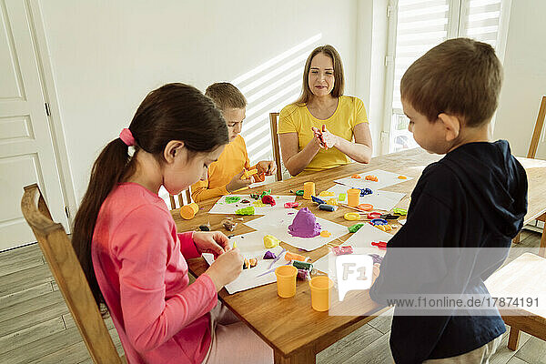 Mutter und Kinder spielen zu Hause mit kinetischem Sand auf dem Tisch