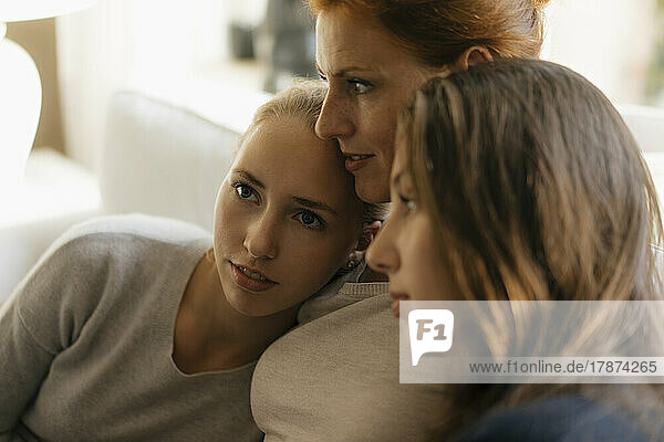 Affectionate mother with two teenage girls on couch at home