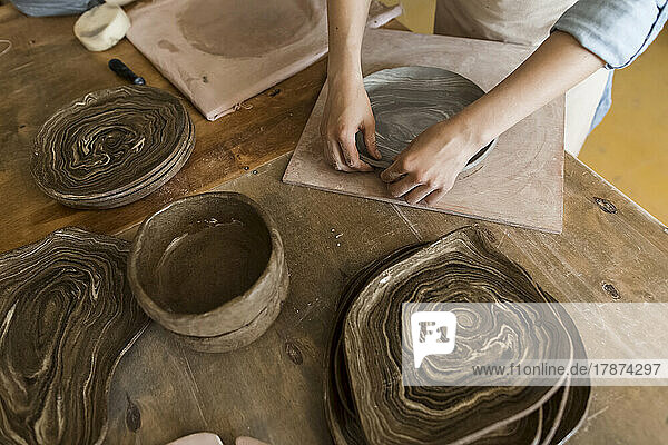 Hands of potter making plate with clay on workbench